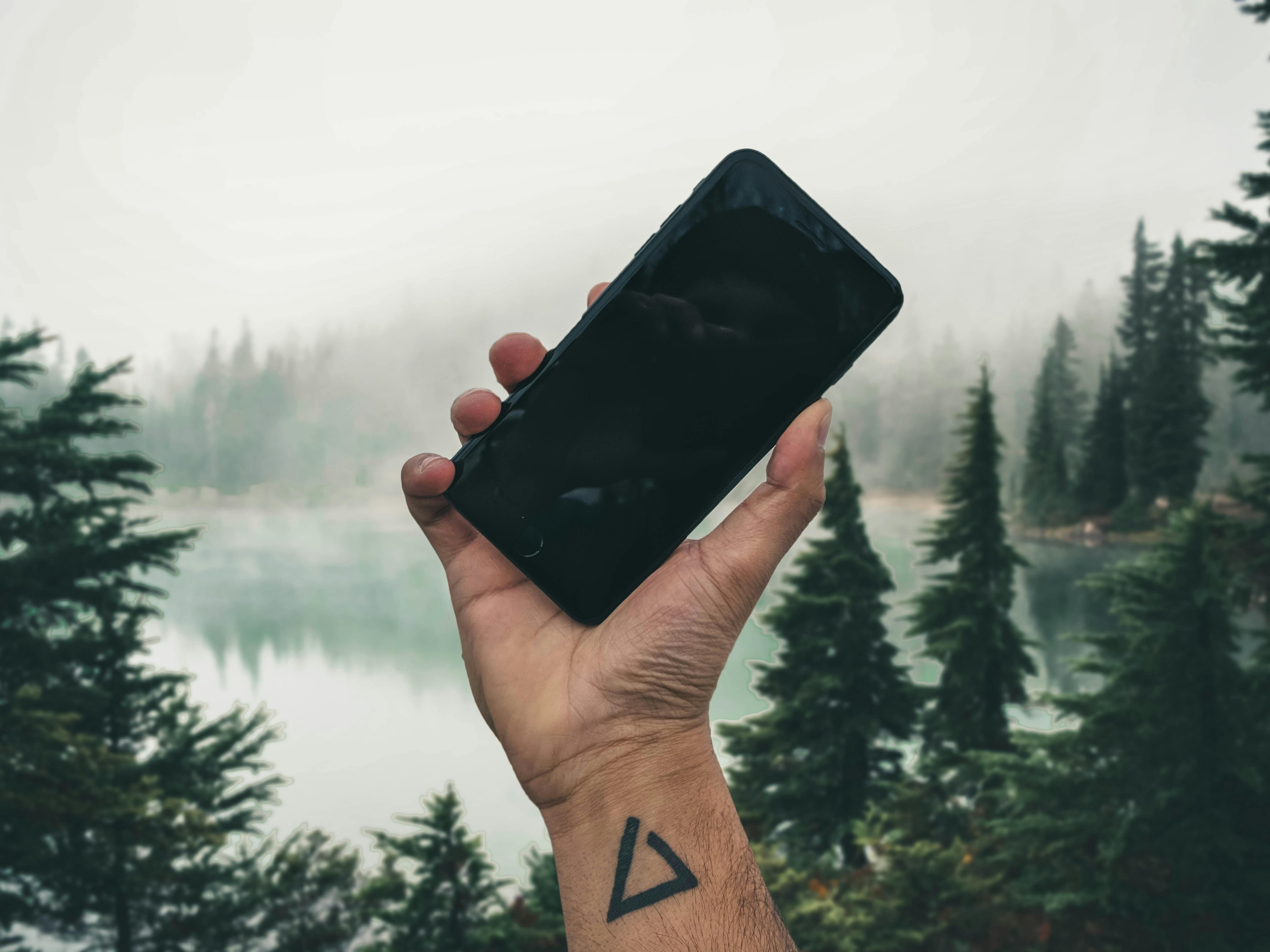 hand holding up a mobile phone in wilderness background