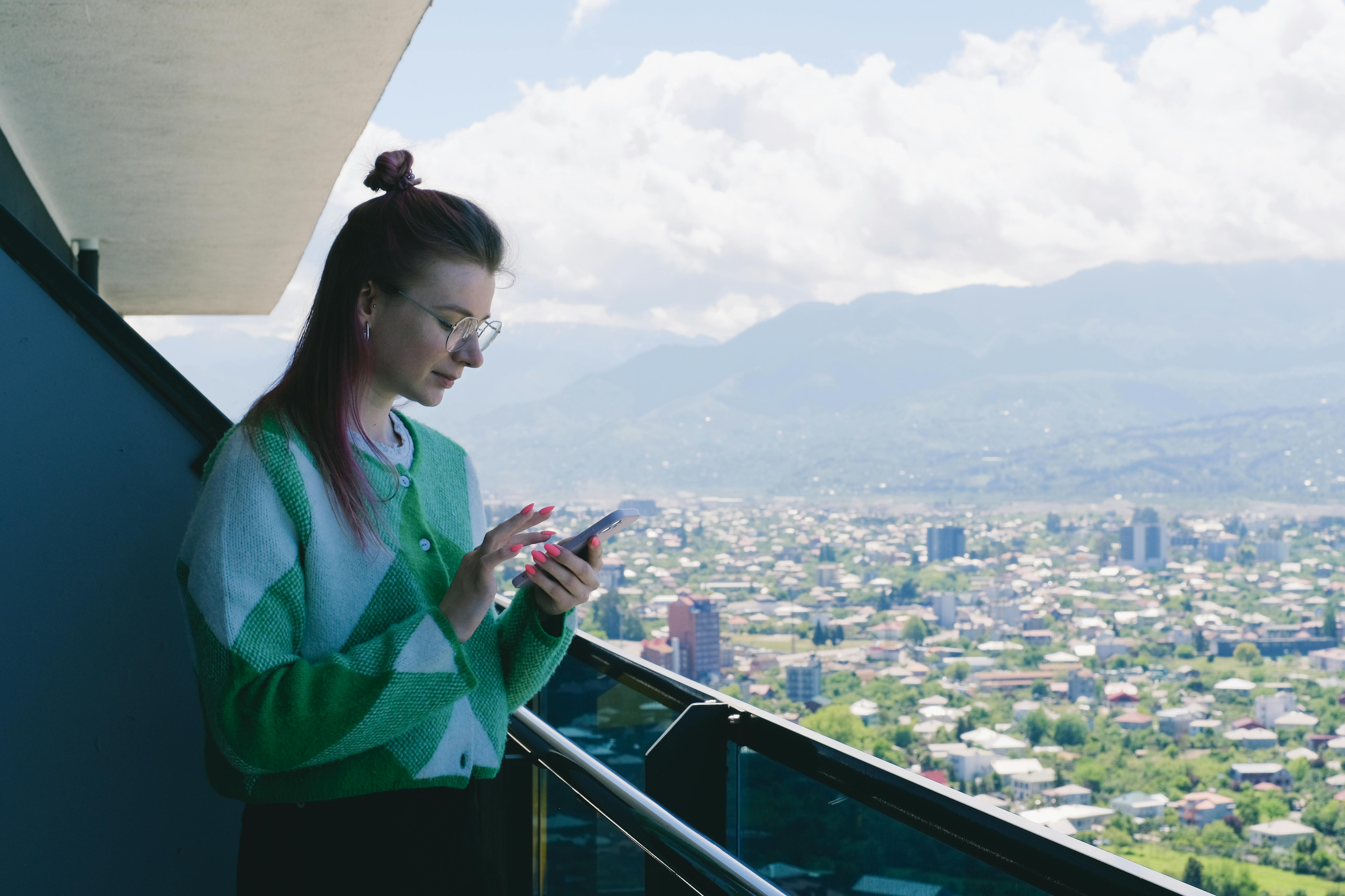 person on mobile phone, standing on balcony overlooking city