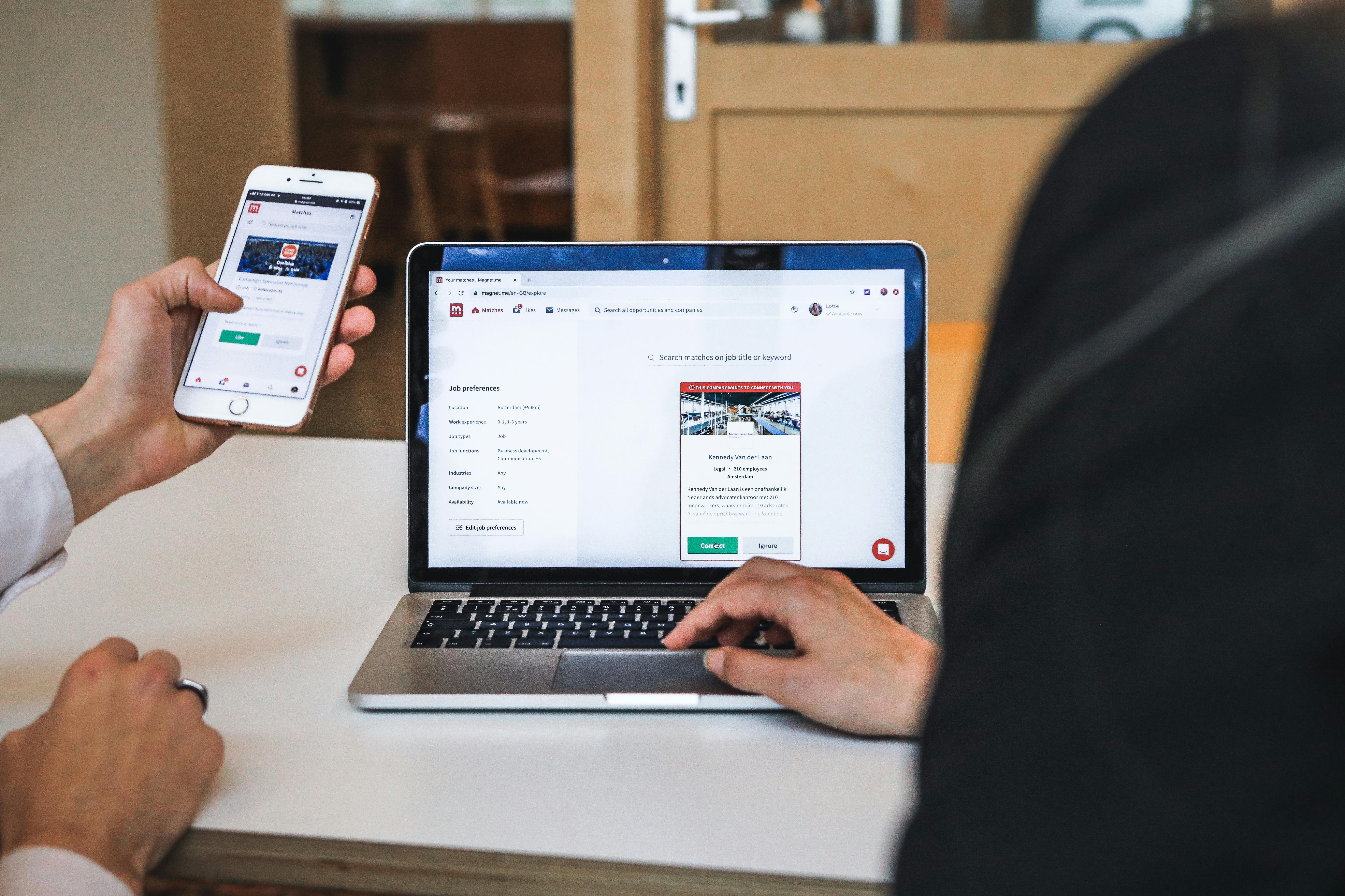 office setting, hand holding a mobile phone, beside an open laptop